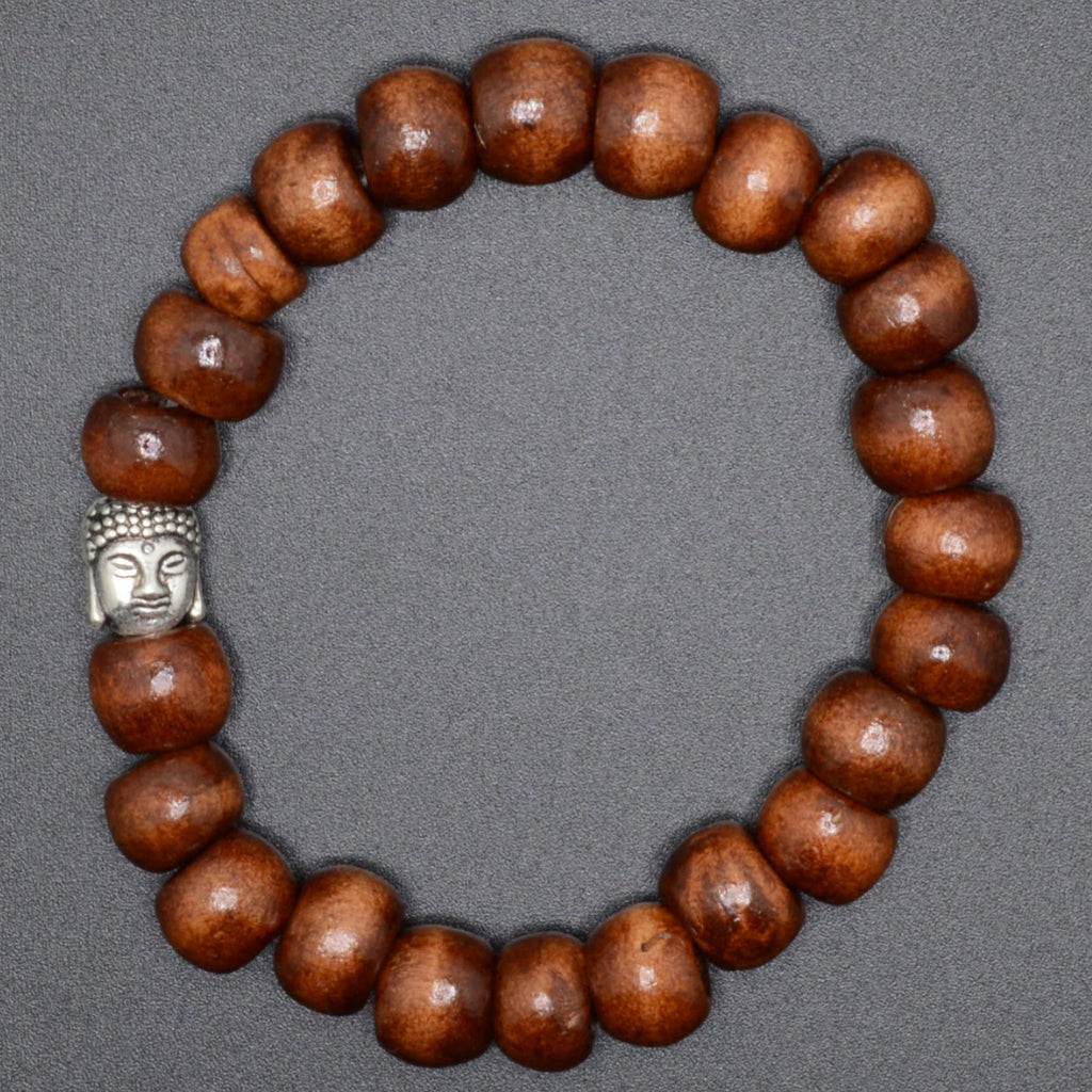 A beaded bracelet made of glossy medium-brown wooden beads with a small silver Buddha head charm, displayed on a neutral gray background.