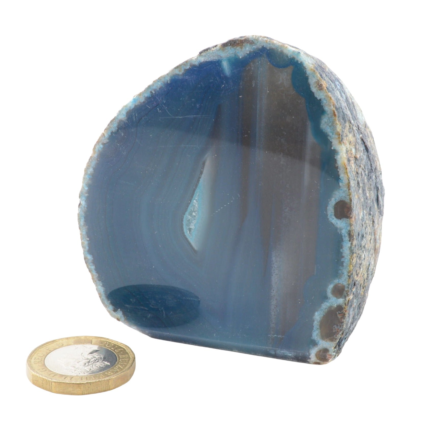 A polished blue agate geode with natural banding and rough crystalline edges, shown on a white background with a coin placed in front for scale.
