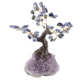 A decorative bonsai-style tree sculpture with blue and white sodalite gemstone leaves, gold-tone wire branches, a brown faux-wood trunk, and an amethyst geode base on a plain white background.