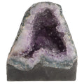 A raw amethyst geode specimen with a dark gray base, featuring light purple and white crystalline outer walls and a deep purple interior, shown on a plain white background.