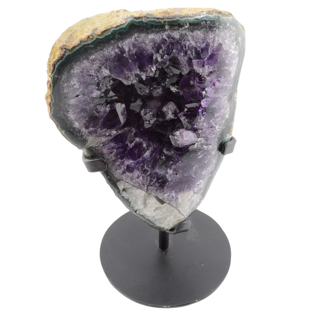 A large amethyst geode specimen with deep purple crystal formations and a natural beige and gray outer matrix, displayed on a black metal stand against a plain white background.