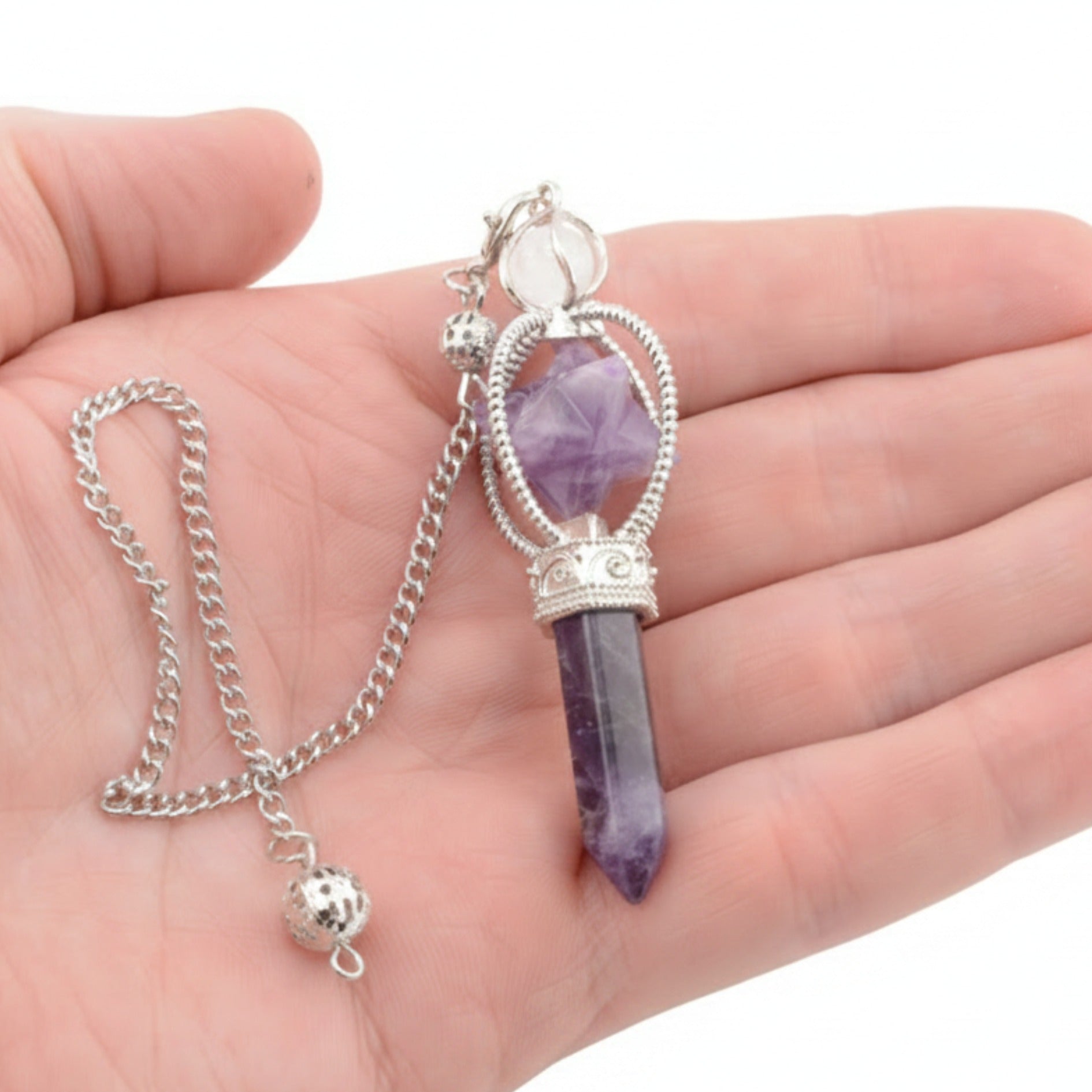 A silver-toned amethyst crystal pendulum with merkaba held in a person's hand against a white background.
