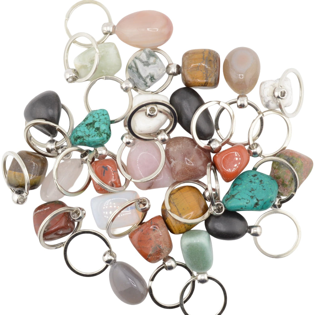 A collection of polished tumbled gemstones in various colors and patterns, each attached to a silver split ring keyring, arranged on a plain white background.