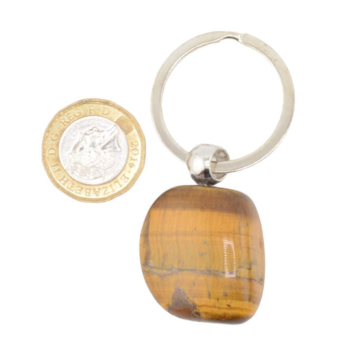 A polished tiger's eye stone keychain with a silver-colored metal split ring keyring, shown next to a British coin for scale on a white background.
