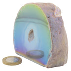 A polished semi-circular aura agate geode with iridescent blue, green, and purple bands, shown on a white background with a coin and circular base for scale.