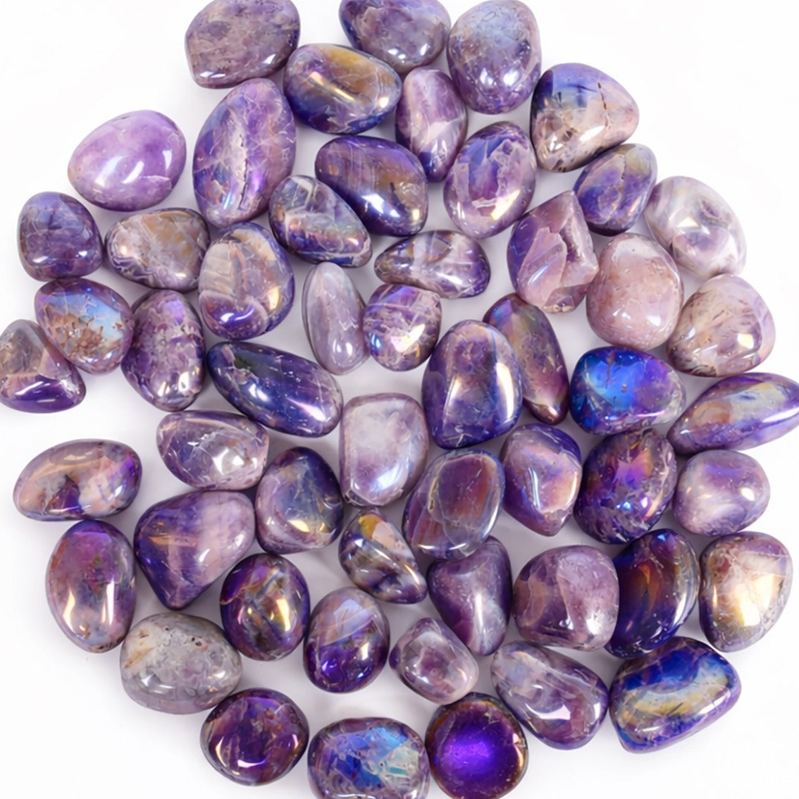 A pile of polished purple tumbled aura amethyst crstal gemstones with iridescent blue, pink, and gold flashes, arranged on a plain white background.