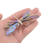 A metallic dragonfly wing ornament with iridescent purple, blue, and gold foil details, resting on a person's palm against a white background.