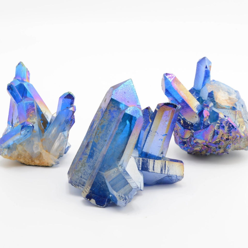 Three blue iridescent crystal clusters with purple and gold highlights, photographed on a clean white background.