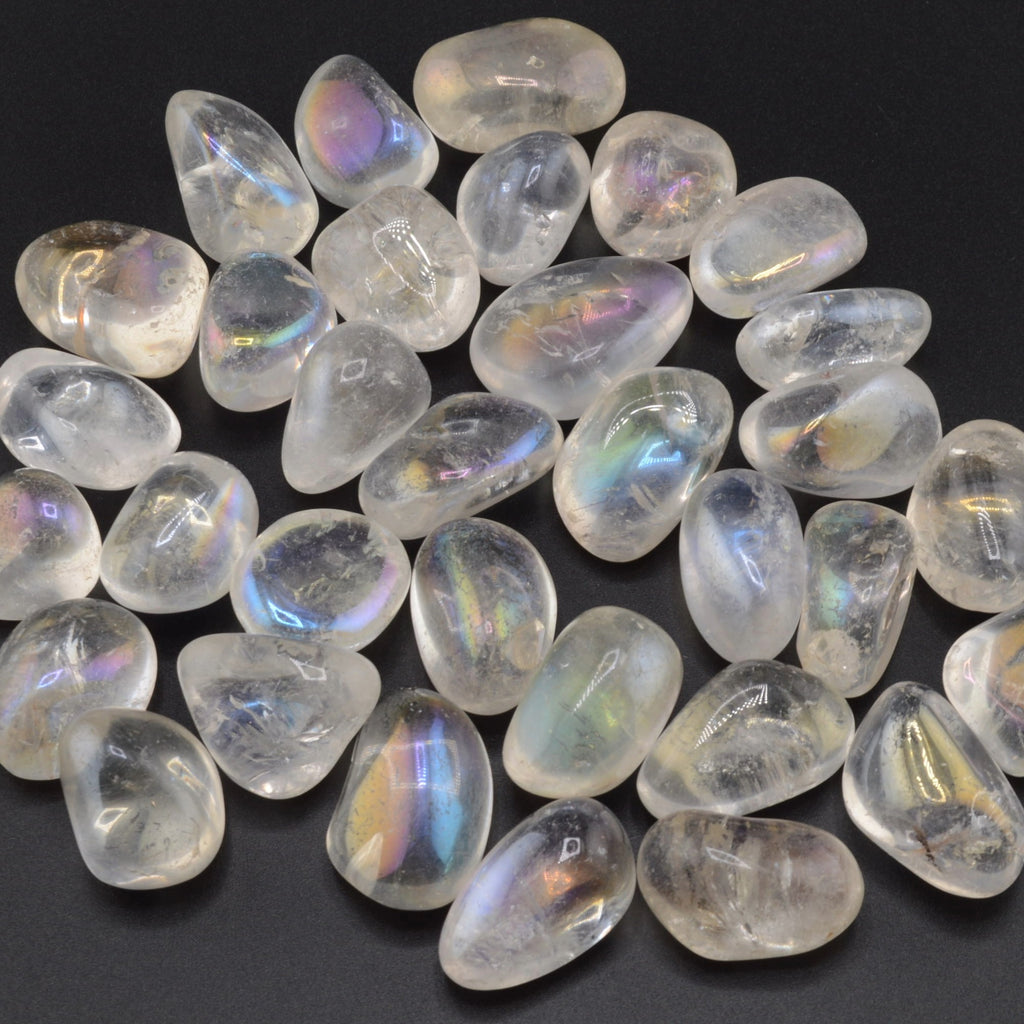 A pile of polished tumbled aura quartz stones with an iridescent rainbow sheen, arranged on a dark black background.