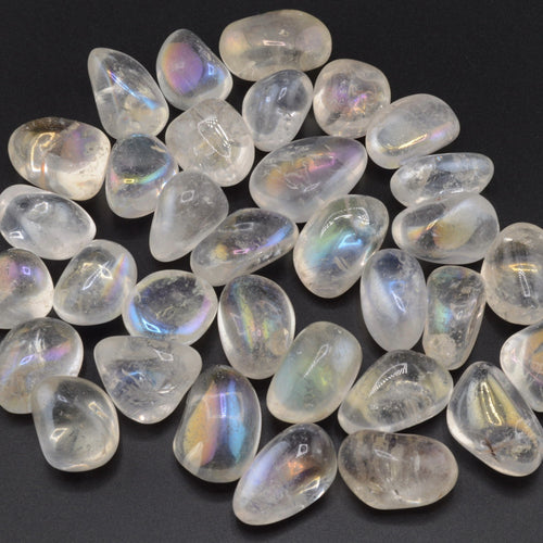 A pile of polished tumbled aura quartz stones with an iridescent rainbow sheen, arranged on a dark black background.