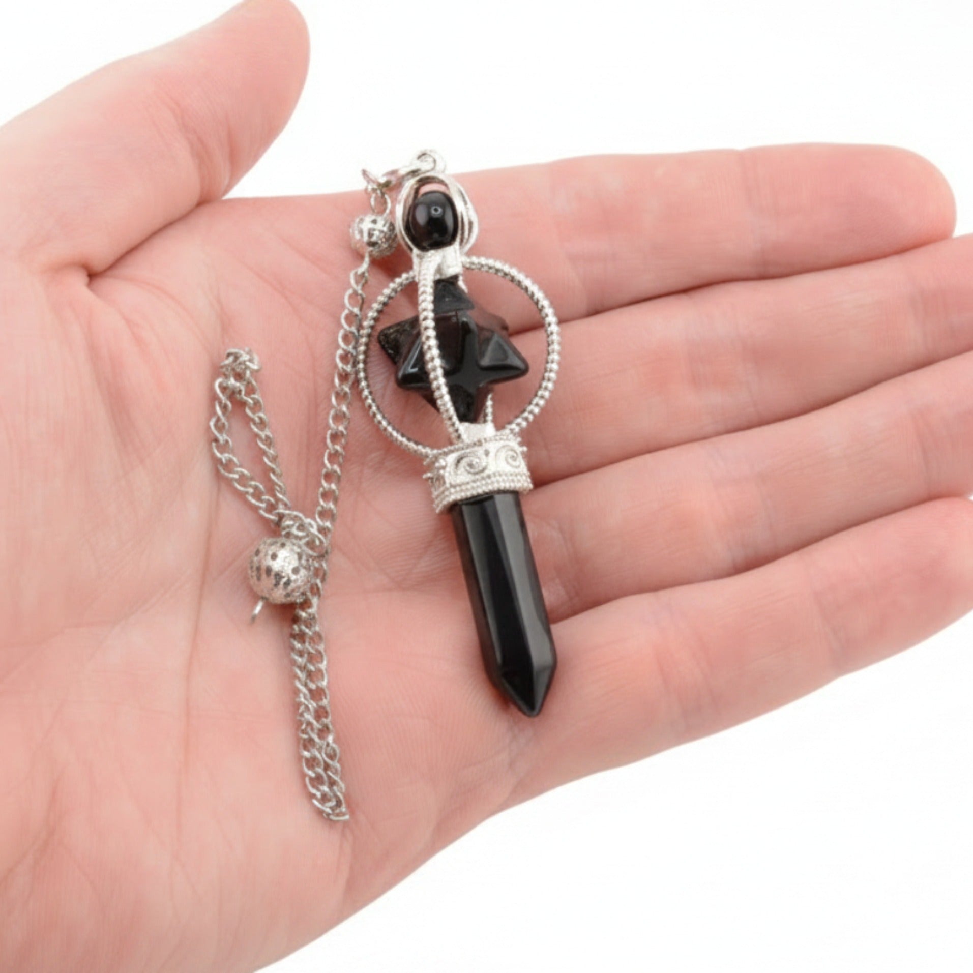 A Black Obsidian Pendulum with a point and merkaba. A hand is holding it on a white background