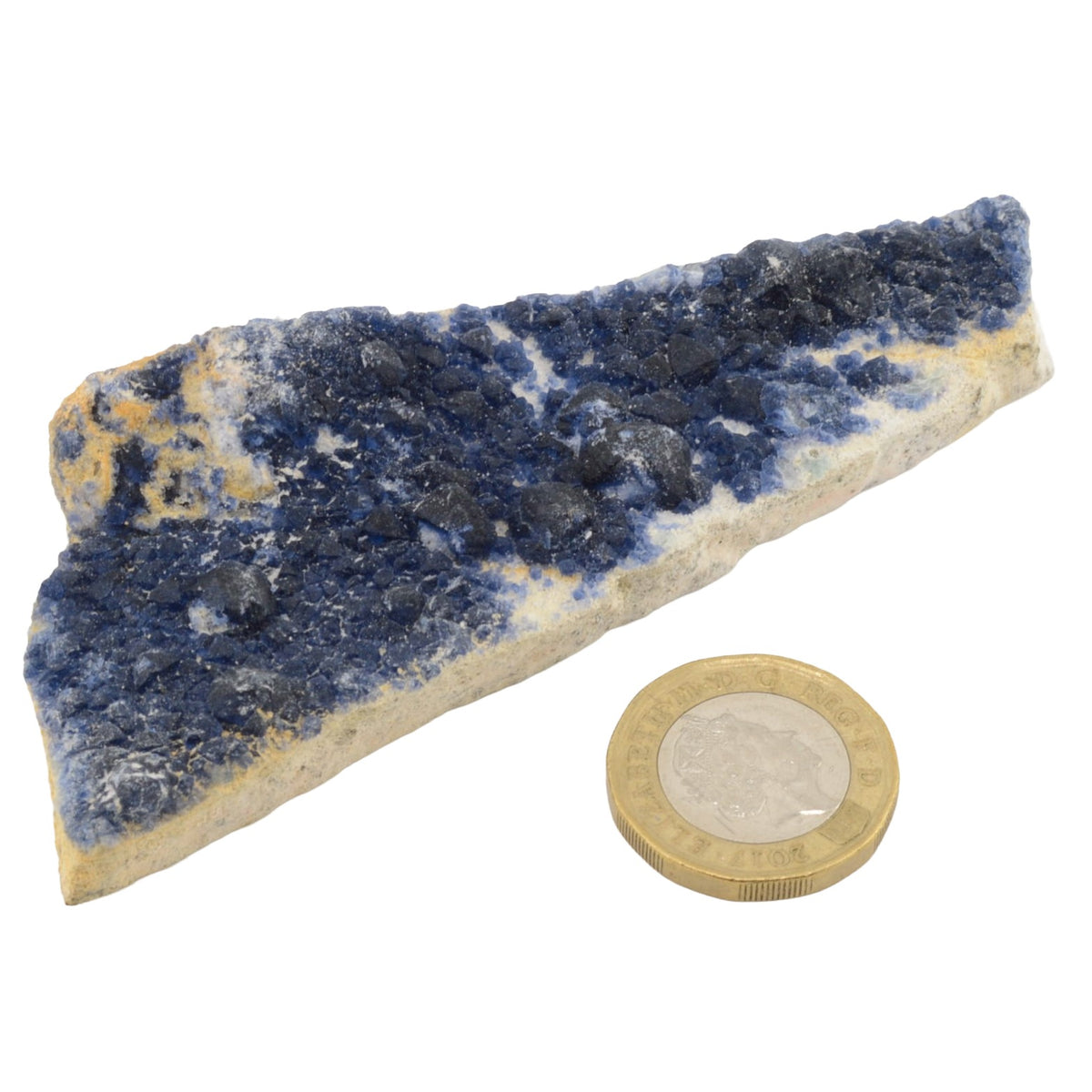 A raw blueberry fluorite specimen displayed next to a British coin for scale, on a white background.
