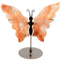 A butterfly-shaped Carving made from orange carnelian crystal wings on a silver metal stand with a round base.