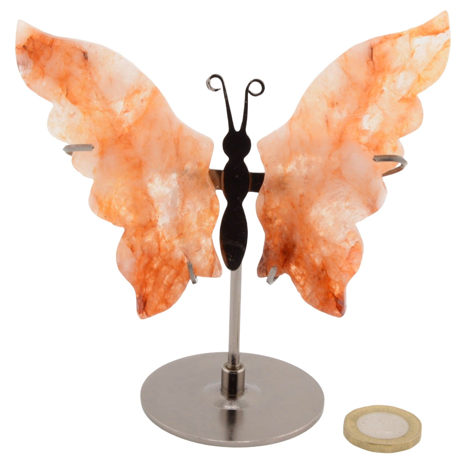 A butterfly-shaped carving made from orange carnelian crystal wings on a silver metal stand, shown against a plain white background with a coin for scale.