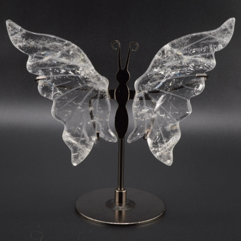 A butterfly-shaped crystal sculpture with clear quartz, inclusions-filled wings mounted on a black metal stand with a round base, photographed against a dark gray background.