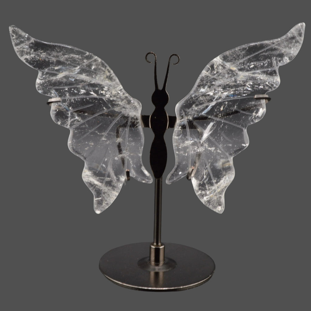 A decorative butterfly-shaped shelf piece with clear quartz crystal wings mounted on a black metal stand with a round base, shown against a dark gray background.