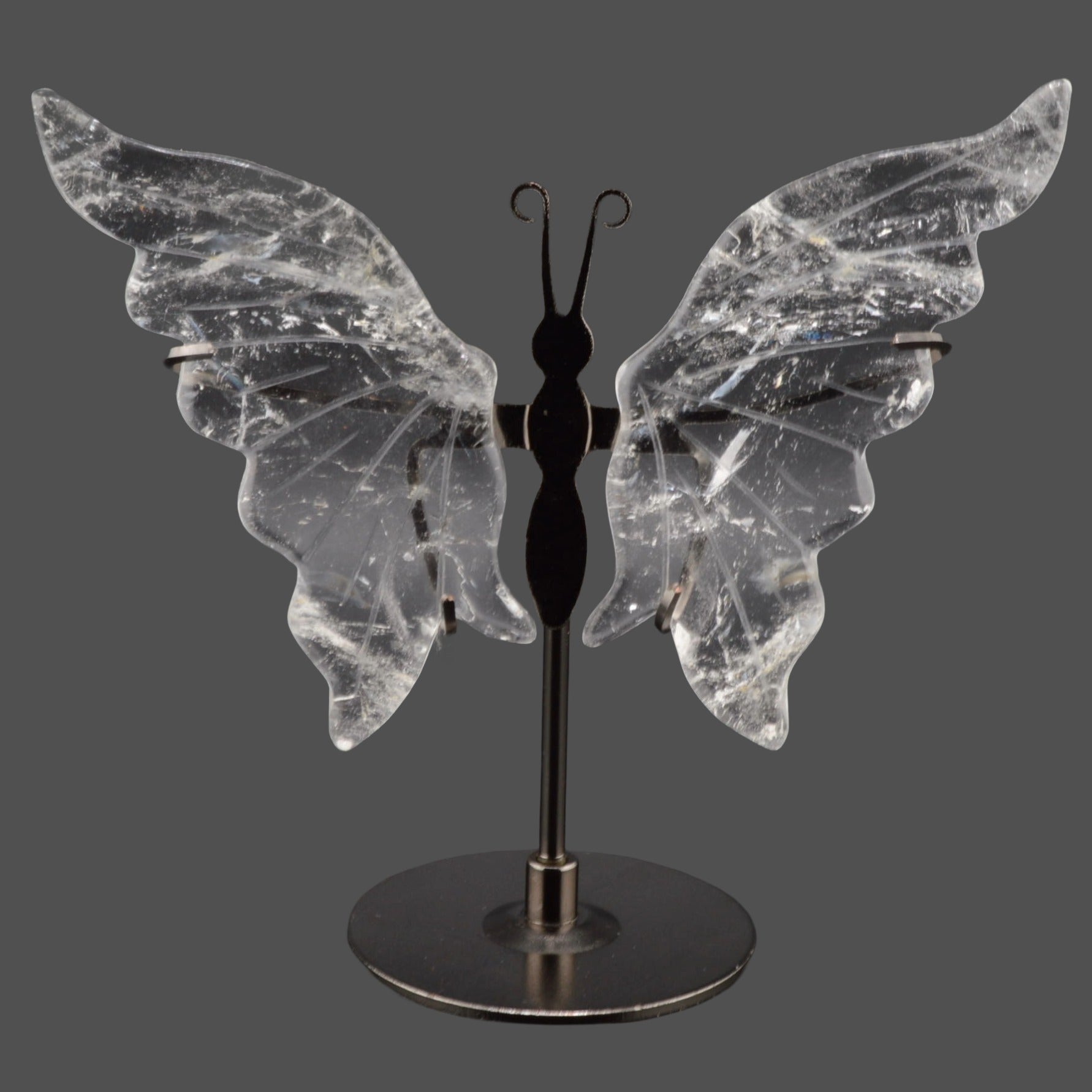 A decorative butterfly-shaped shelf piece with clear quartz crystal wings mounted on a black metal stand with a round base, shown against a dark gray background.