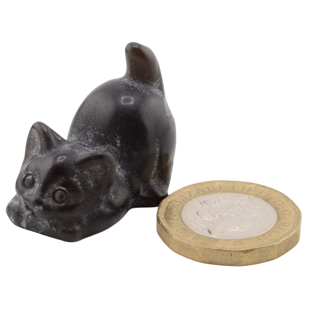 A small black cat figurine posed beside a British coin for scale, on a plain white background.