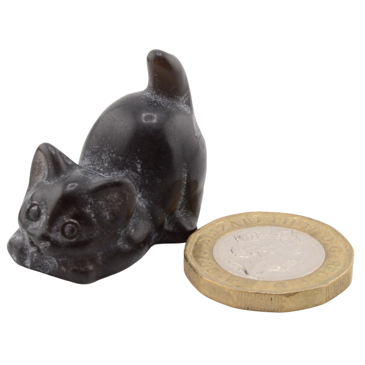 A small black cat figurine posed beside a British coin for scale, on a plain white background.