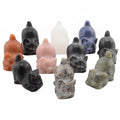 A group of small carved gemstone cat figurines in multiple natural stone colors, including black, pink, blue, orange, white, gray, and green, arranged on a plain white background.