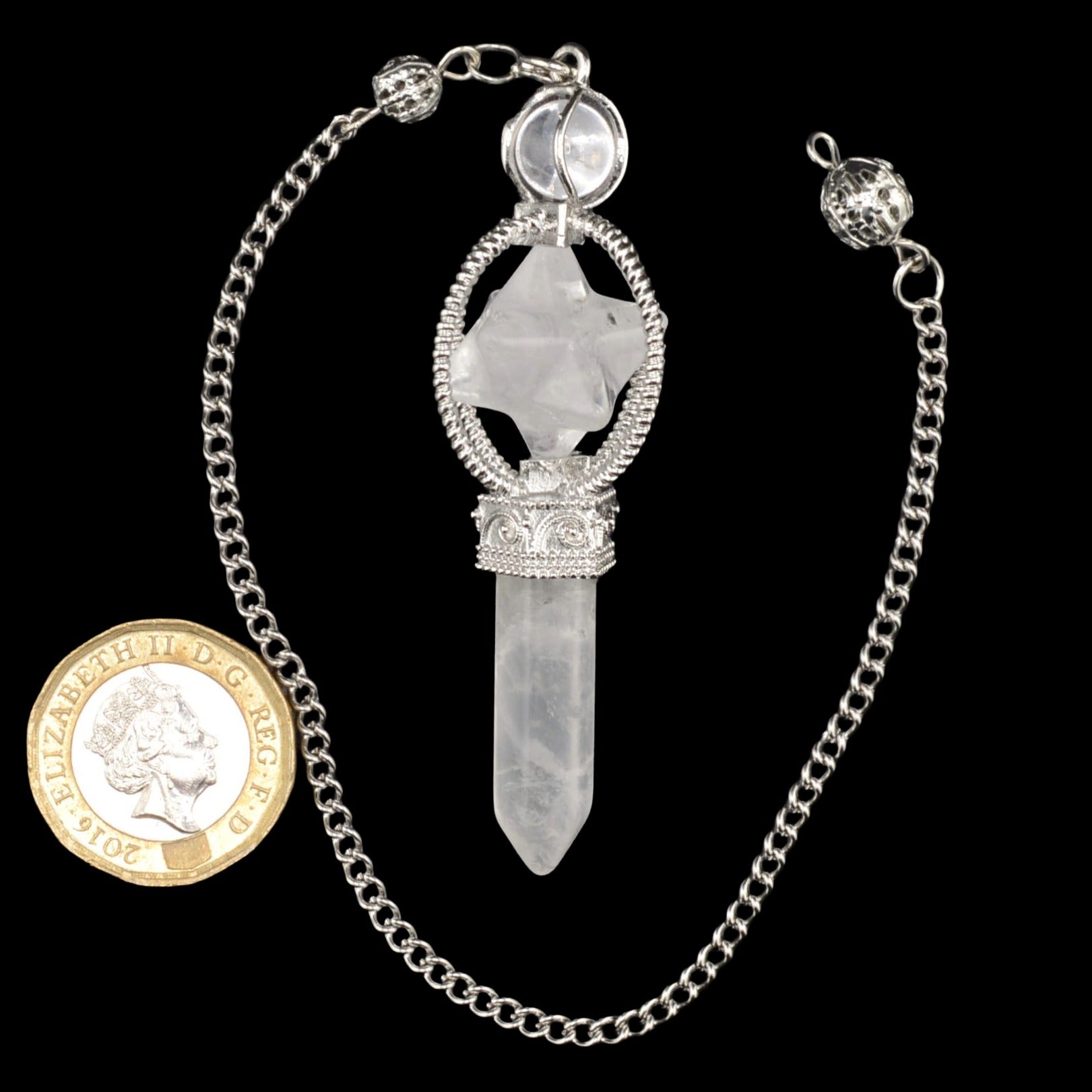 A silver-toned chain necklace featuring a clear quartz crystal point pendulum with a merkaba, displayed next to a gold coin for scale against a solid black background.