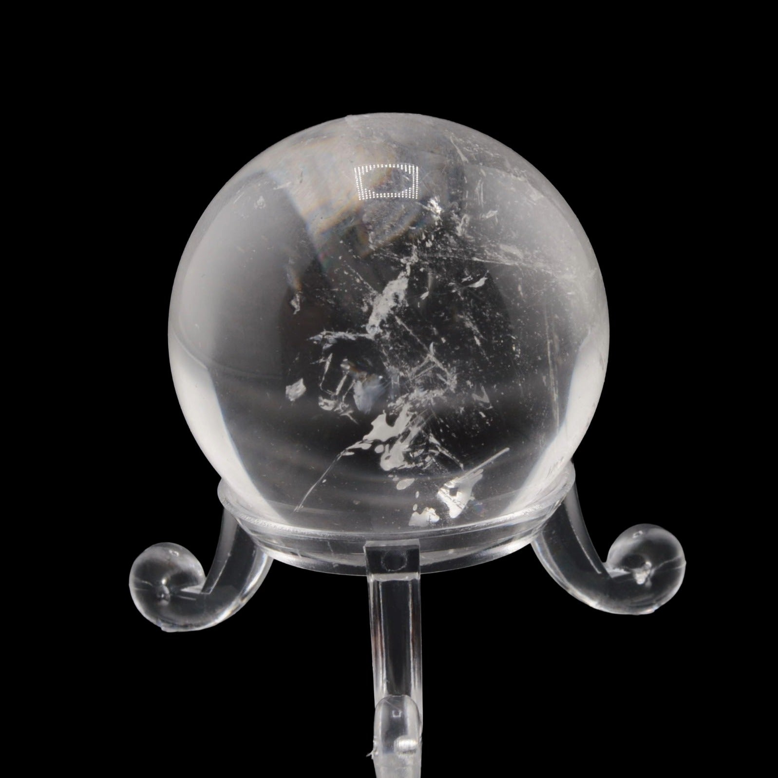 A clear quartz crystal sphere with visible internal inclusions and swirls, displayed on a transparent stand against a solid black background.