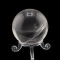 A clear quartz crystal sphere on a matching clear display stand, photographed against a solid black background.