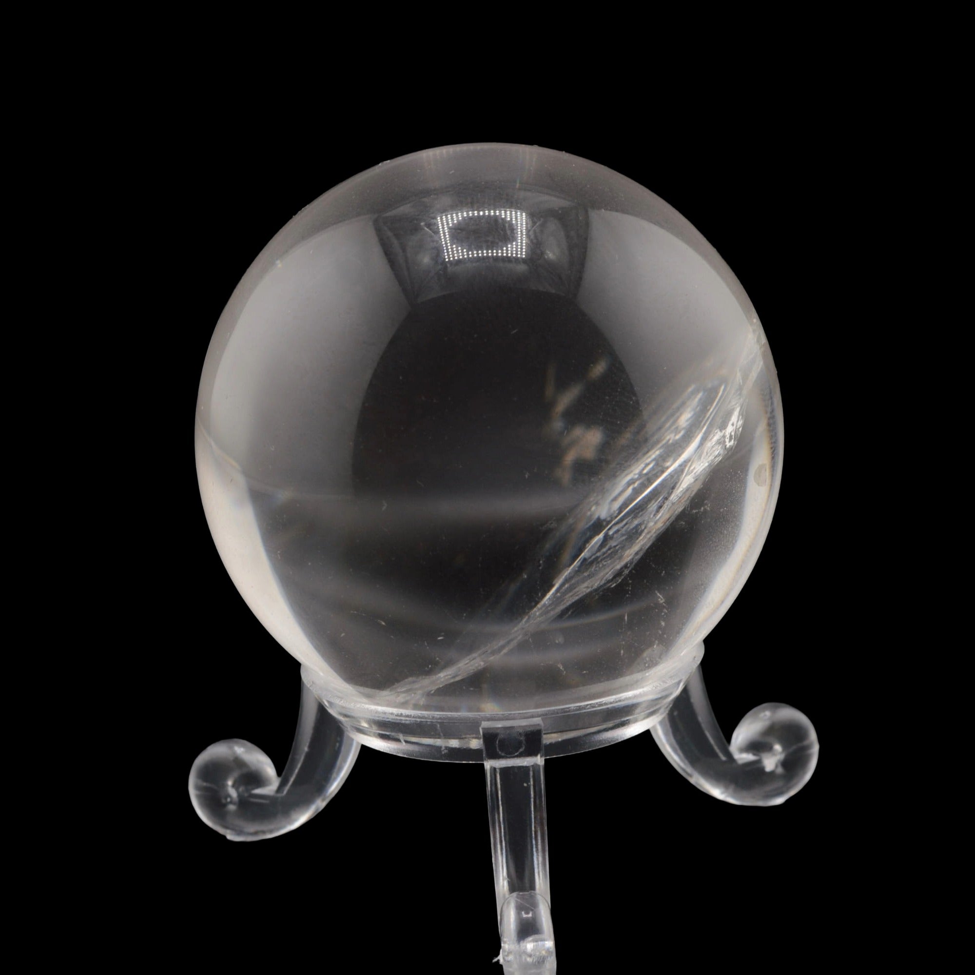 A clear quartz crystal sphere on a matching clear display stand, photographed against a solid black background.