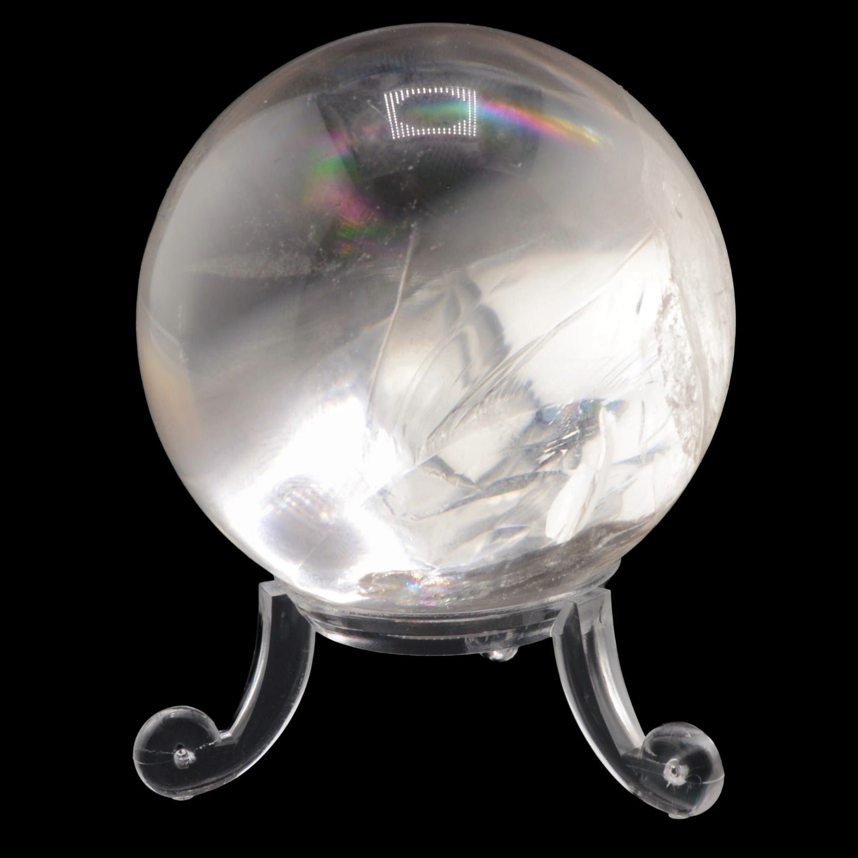 A clear quartz crystal ball with natural inclusions and internal feather-like structures, displayed on a transparent acrylic stand against a solid black background.