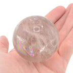 A translucent clear quartz crystal sphere with rainbow, held in a person's hand against a plain white background.
