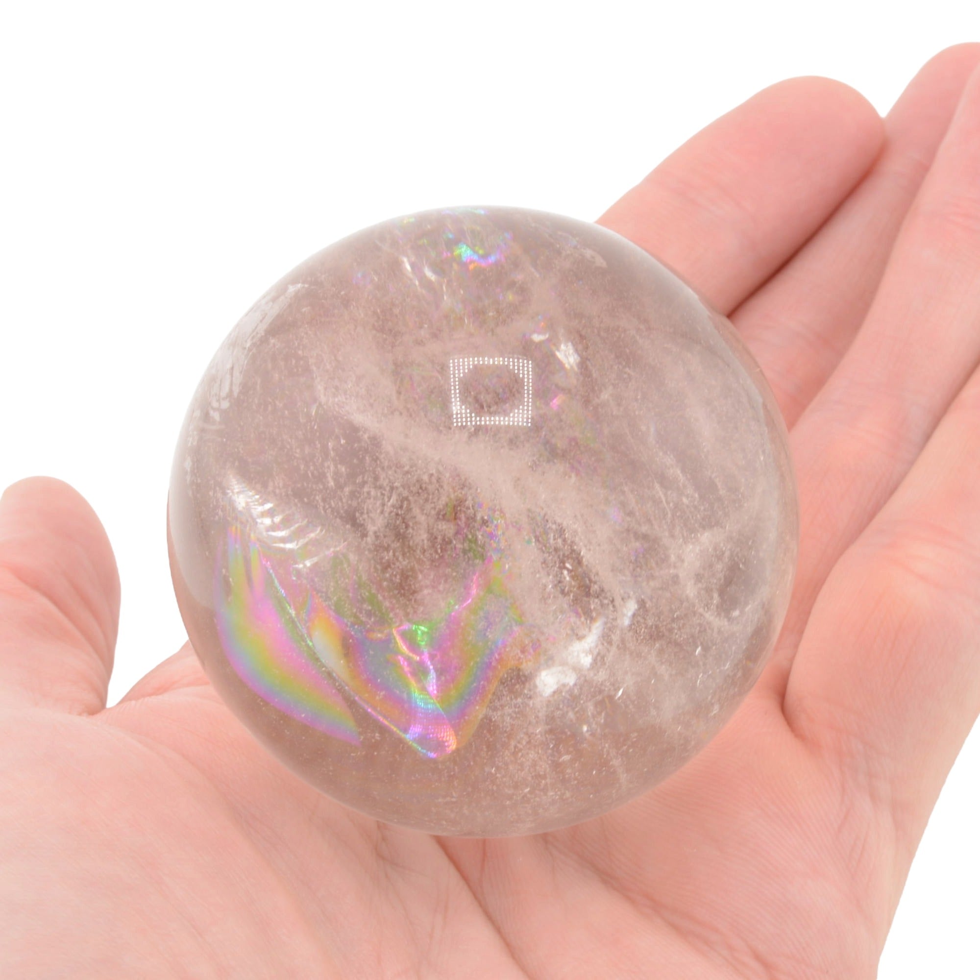 A translucent clear quartz crystal sphere with rainbow, held in a person's hand against a plain white background.