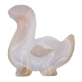 A small carved figurine of a dinosaur made from polished druzy agate, featuring natural banding in shades of off-white, pale pink, and cream, set against a plain white background.