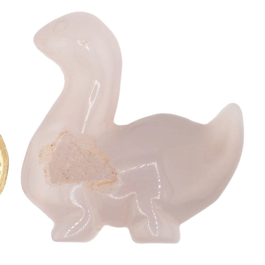 A small dinosaur carving made from druzy agate in a milky translucent pale pink, filled with embedded glitter, shown on a plain white background.