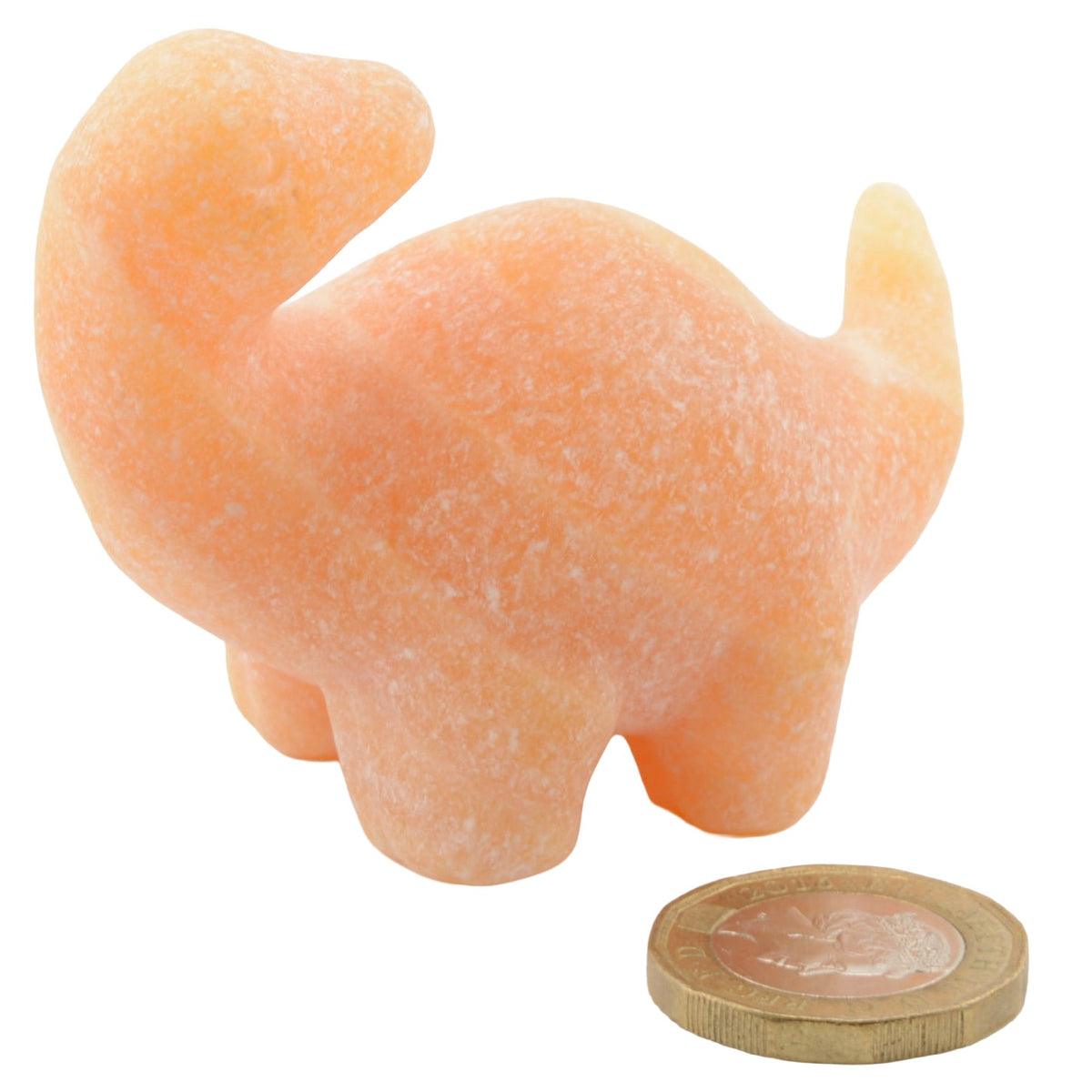 A small carved figurine of a dinosaur creature in a peachy orange calcite gemstone, shown next to a coin for scale on a white background.