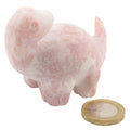 A small carved pink opal gemstone dinosaur figurine, shown on a plain white background with a coin placed in front for scale.