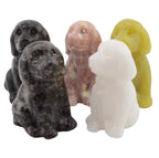 Five small dog-shaped gemstone figurines in different colors: black, dark gray speckled, pinkish beige, and pale yellow, arranged on a white background.