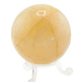 A polished yellow-orange golden healer quartz crystal sphere resting on a clear acrylic display stand, isolated on a white background.