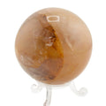 A polished orange-brown golden healer quartz sphere on a clear acrylic display stand, set against a plain white background.