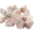 A pile of rough, unpolished pink sodalite which is known as hackmanite on a plain white background.