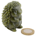 A small green hedgehog figurine shown on a plain white background, with a UK one-penny coin placed in front for scale.