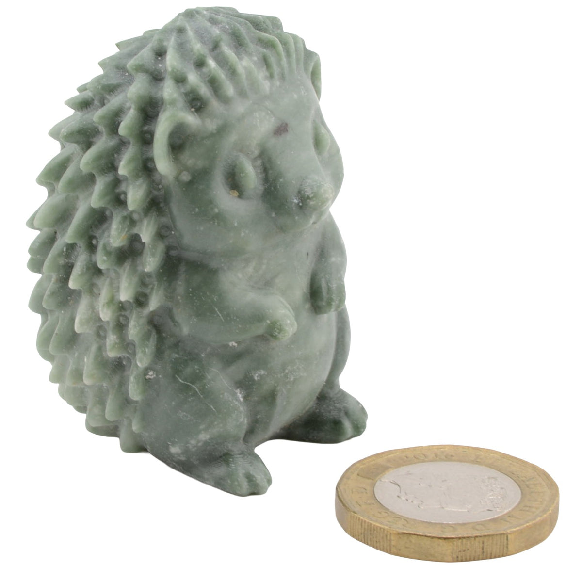 A small green stone hedgehog figurine shown next to a UK 10-pound coin for scale, on a plain white background.