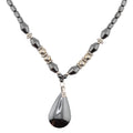 A beaded necklace featuring faceted dark gray heamatite crystal beads, small metallic silver beads, and a large teardrop-shaped dark gray haematite pendant with a silver geometric accent.