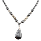 A beaded necklace featuring faceted dark gray heamatite crystal beads, small metallic silver beads, and a large teardrop-shaped dark gray haematite pendant with a silver geometric accent.