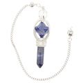 A silver-toned chain pendulum featuring a pendant with a faceted blue lapis lazuli crystal and a polished blue crystal point, set in silver-toned metal on a white background.