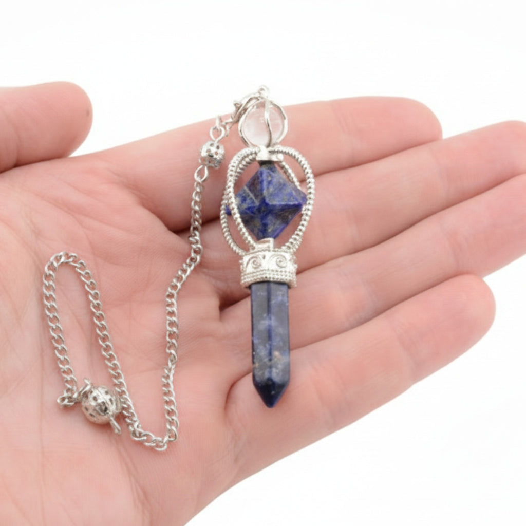 A silver-toned pendulum featuring a faceted dark blue lapis lazuli crystal point, displayed resting on an open hand against a white background.