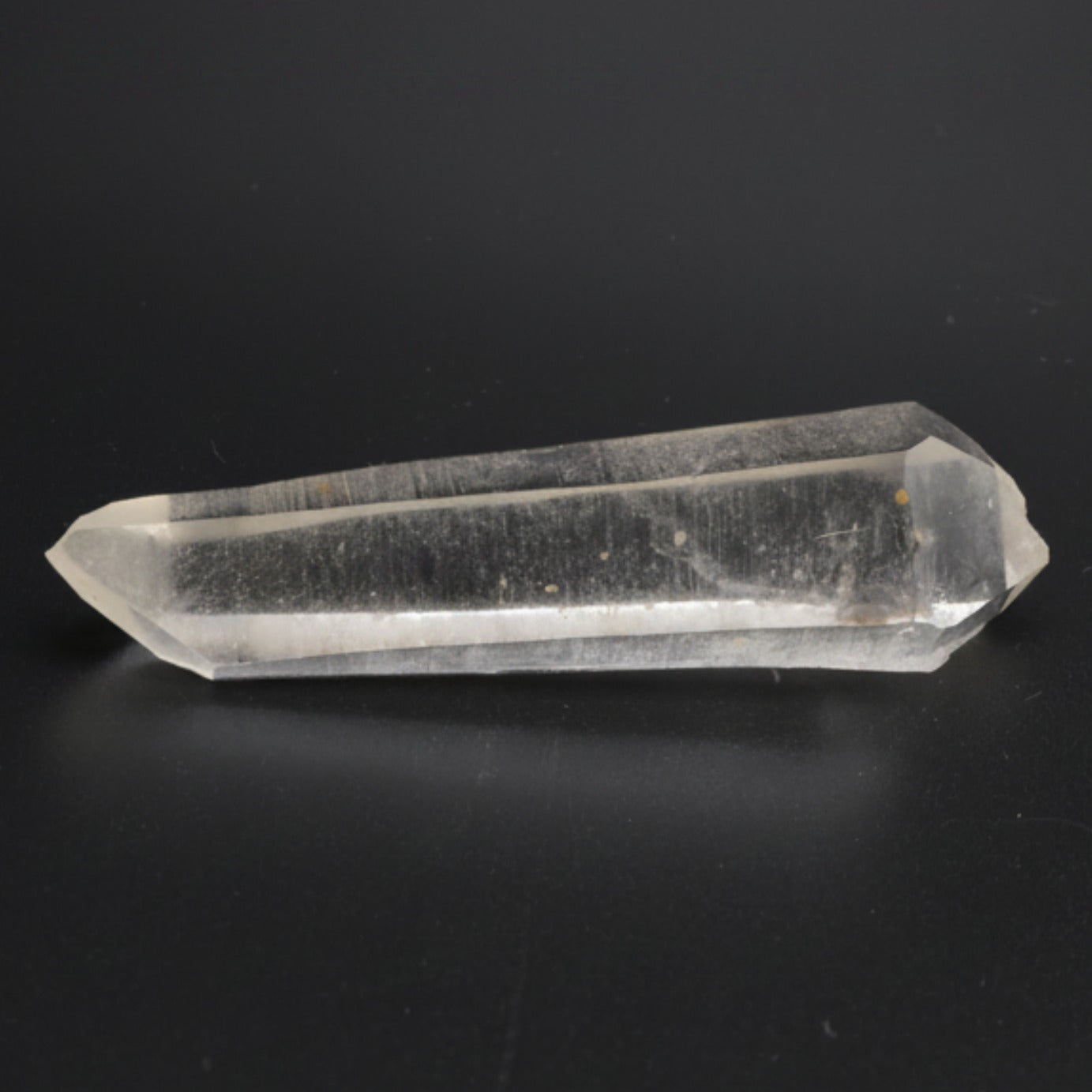 A clear laser quartz crystal point with a hexagonal shape, resting on a dark black background.