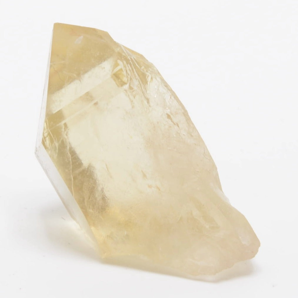 A raw, rough-cut citrine crystal mineral specimen with natural facets, showing a pale yellow color and internal inclusions, photographed on a seamless white background.