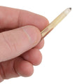 A close-up of a hand holding a small, translucent yellow citrine crystal point against a solid white background.