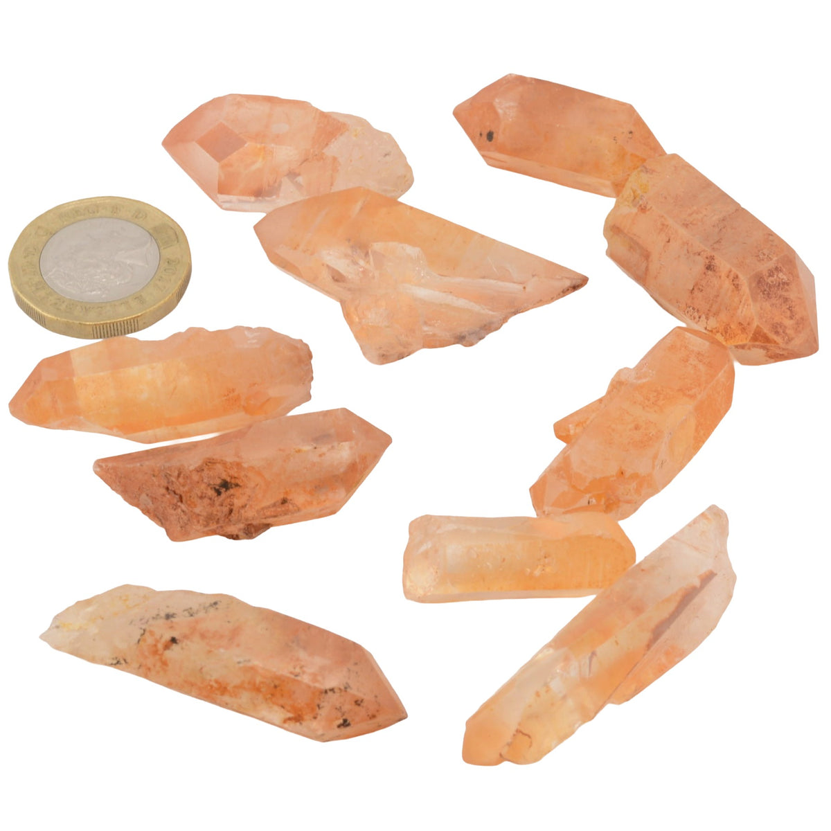 Ten raw tangerine quartz crystal points arranged on a white background next to a British coin for scale.