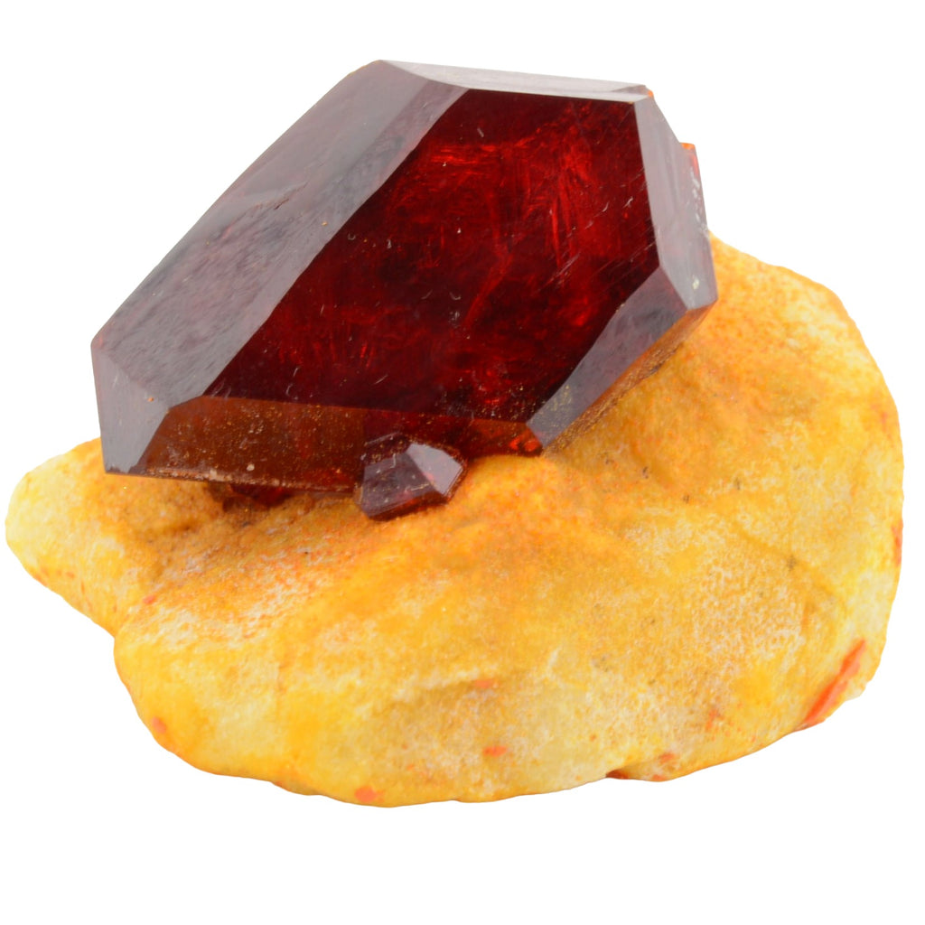 A faceted dark red pruskite crystal displayed on a textured yellow-orange rock base against a plain white background.